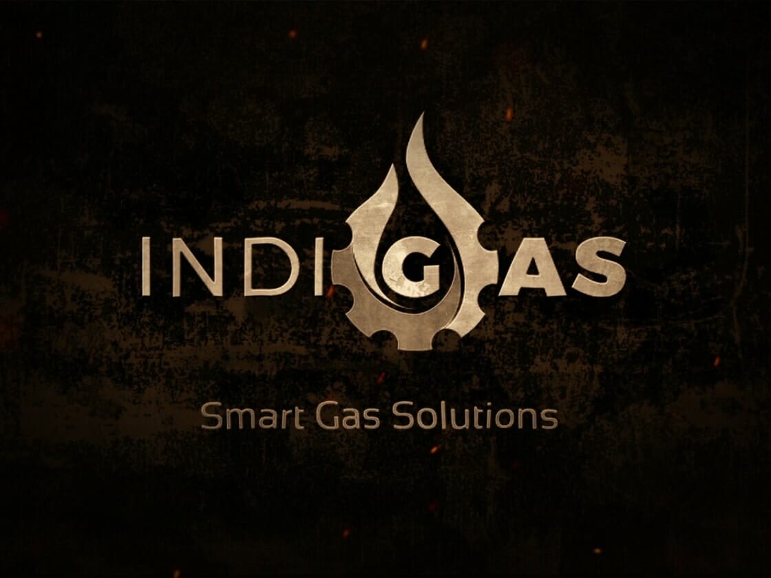 The image features the logo for "IndiGas," a company providing smart gas solutions. The logo consists of the word "INDIGAS," with the "G" stylized as a gas flame with a gear incorporated at the base. Below the logo, the tagline "Smart Gas Solutions" is written. The background is dark and textured.