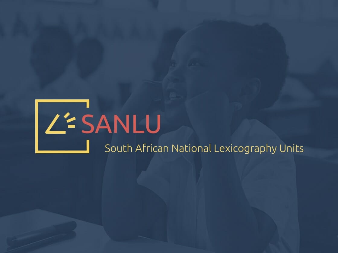 A young child in a classroom smiles while sitting at a desk. The image has a dark blue overlay with the logo and text of SANLU (South African National Lexicography Units) prominently displayed in the foreground. The logo is yellow with a stylized book and arrow design.
