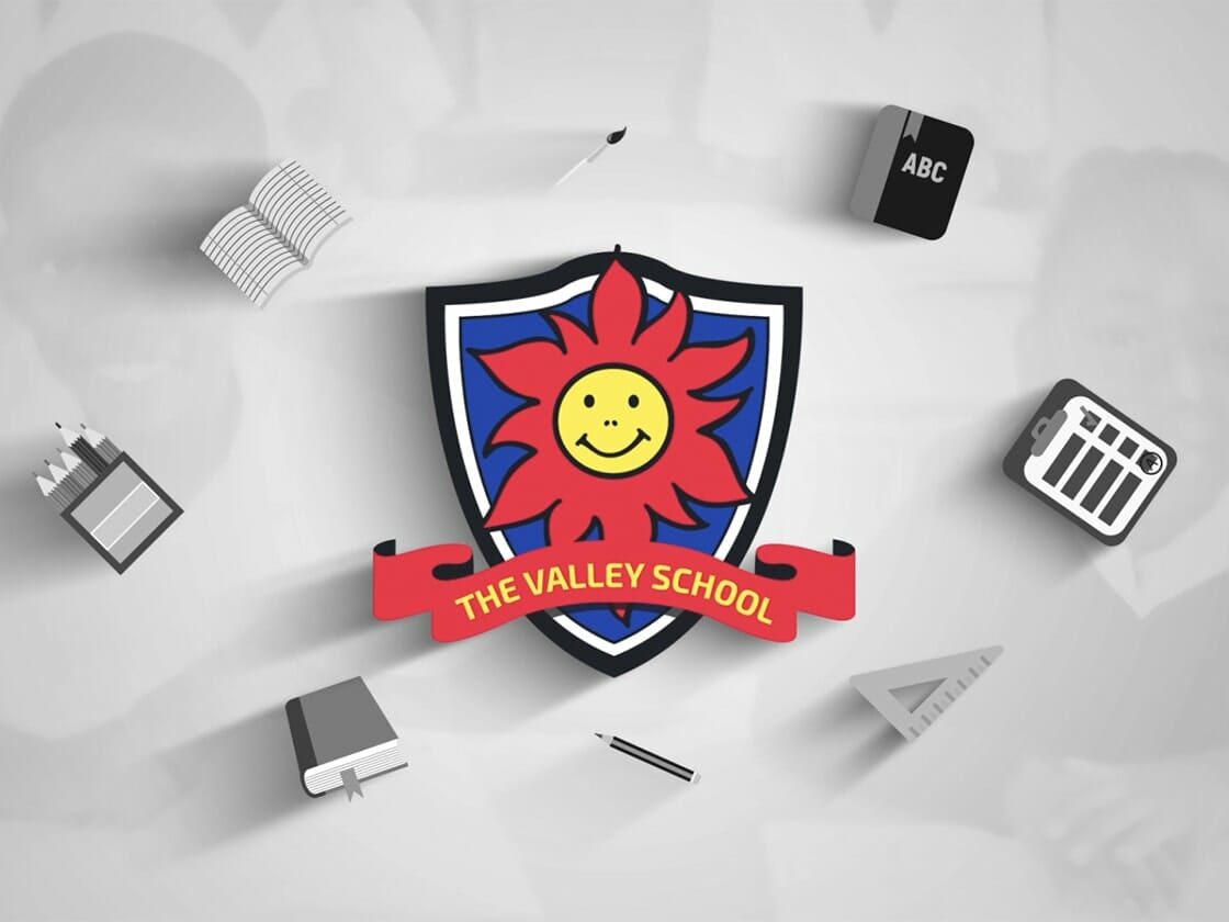 A colorful emblem with a smiling sun face at the center, surrounded by a blue shield with a red outline. Below the emblem is a red banner reading "The Valley School." Around the emblem, grayscale icons depict a book, building blocks labeled "ABC," a calendar, pencils, and a notepad.