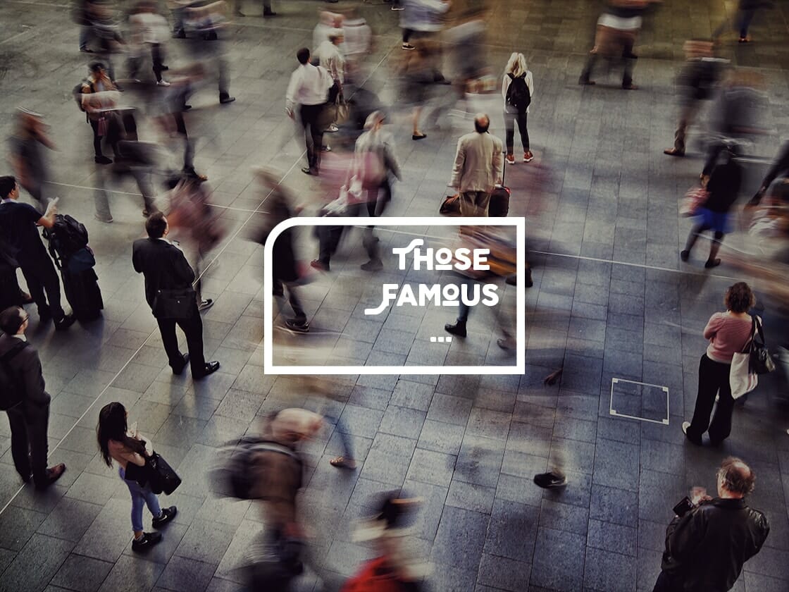 A blurry, high-angle shot of a busy public area where numerous people are walking or standing. The image's motion effect captures the hustle and bustle of the crowd. In the center of the image, white text in a speech bubble reads, "THOSE FAMOUS ...". The ground is paved with large, dark tiles.