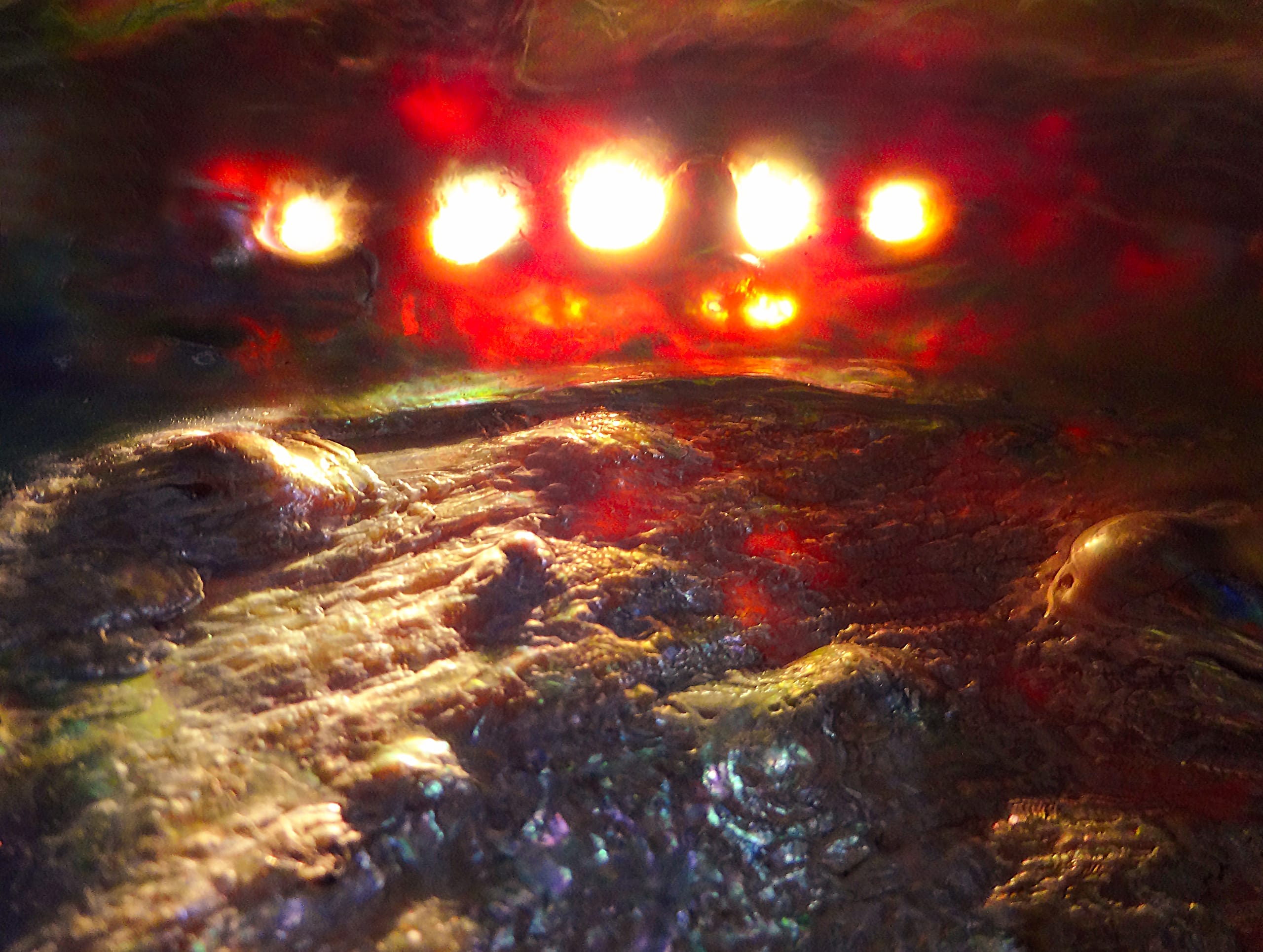An abstract image with a textured, colorful surface resembling a rocky landscape. Bright, glowing orbs hover near the top, casting red and orange hues. The lower section features rough textures with hints of blues and purples, evoking an otherworldly scene.