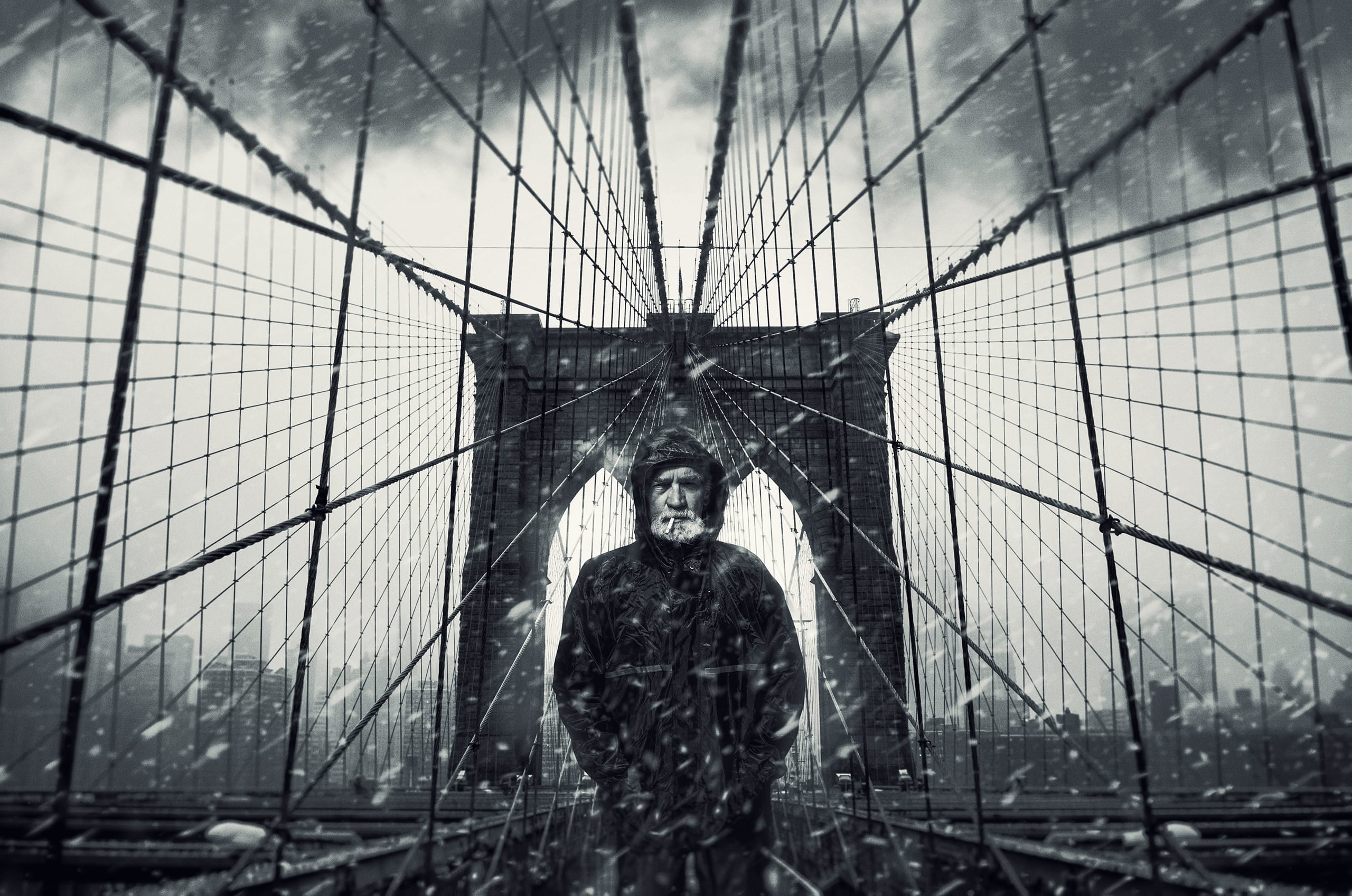 A person stands on the Brooklyn Bridge during a snowy day. The scene is in black and white, creating a dramatic and moody atmosphere. The geometric lines of the bridge's cables converge towards the figure in the center, who is dressed in a dark winter coat and hat. Snowflakes are visible in the air.