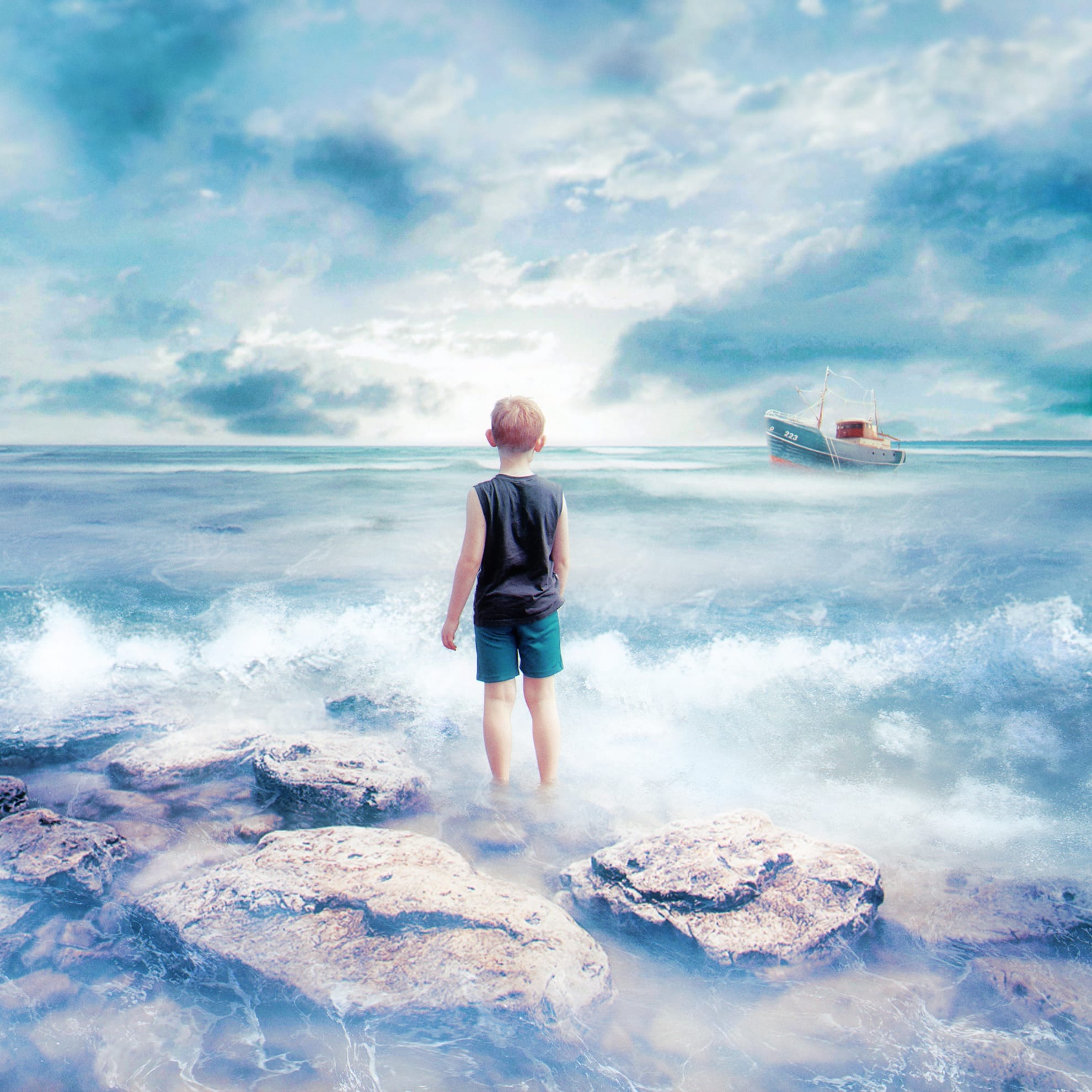A young boy stands barefoot on the rocky shore, facing the ocean under a partly cloudy sky. He wears a sleeveless shirt and shorts. Gentle waves touch his feet. In the distance, a small boat floats on calm waters. The scene has a dreamy, surreal quality like an award-winning piece of artwork in a magazine.