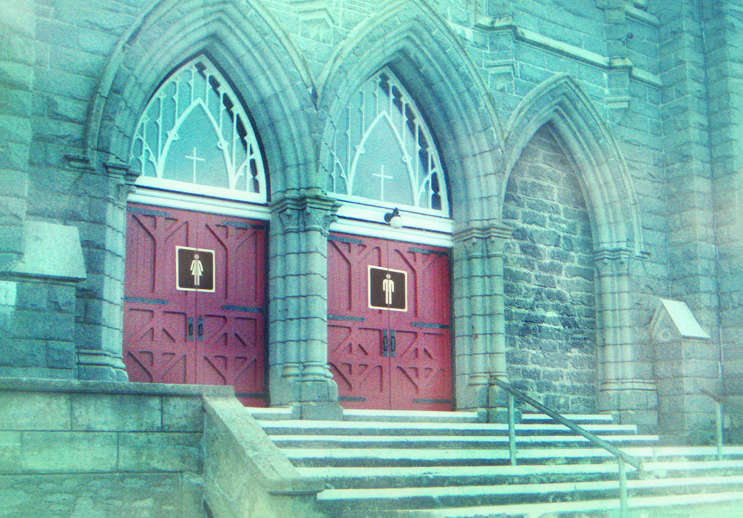 Two red doors with gender-specific restroom signs are located at the top of a set of stone steps on a Gothic-style building. The male and female symbols adorn the left and right doors respectively, while a third door stands between them. Arched windows and intricate stone architecture highlight where you find this unique building.