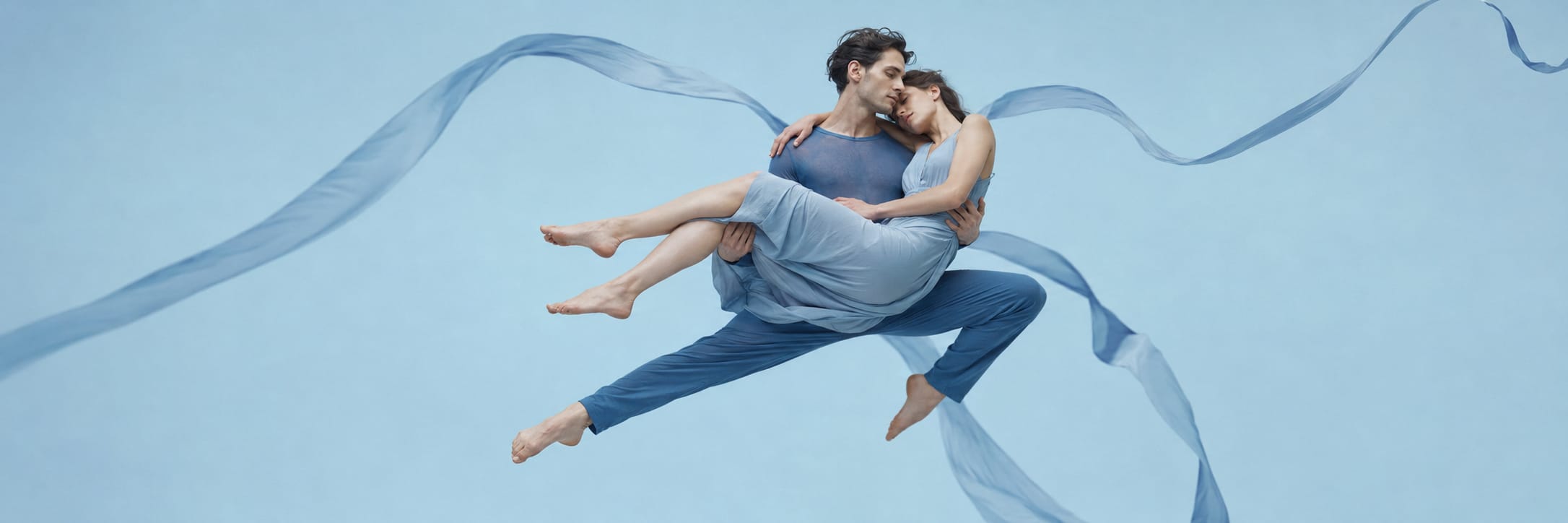 Two dancers in blue leap with swirling ribbons, showcasing a surreal display of strength and spirit.