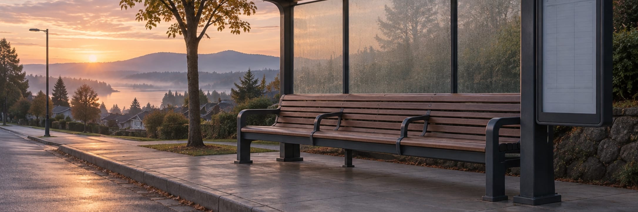 An empty bus stop and long bench sit beneath a pink dawn sky.